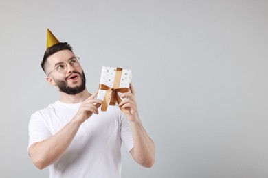 Photo of Happy Birthday. Handsome man with party hat and gift box on grey background, space for text