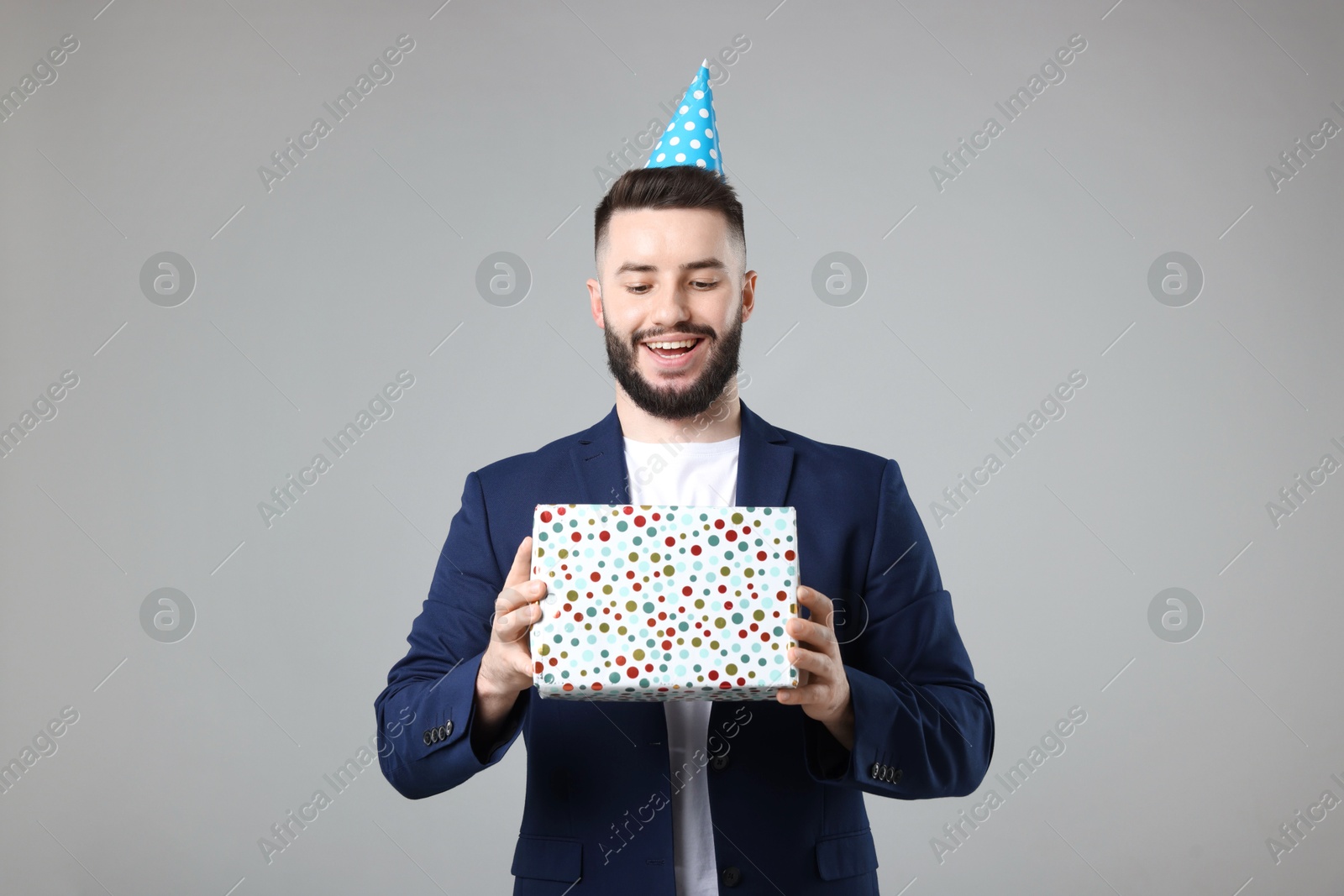 Happy Birthday. Handsome man with party hat and gift box on grey background Photo of Happy Birthday. Handsome man with party hat and gift box on grey background