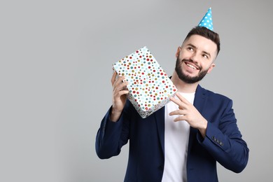 Photo of Happy Birthday. Handsome man with party hat and gift box on grey background, space for text