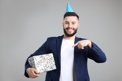 Photo of Happy Birthday. Handsome man with party hat and gift box on grey background