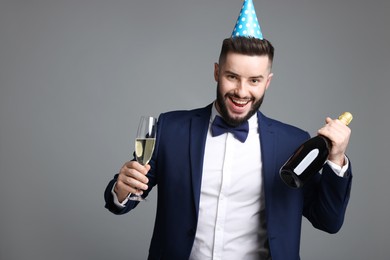 Photo of Happy Birthday. Handsome man with party hat and champagne on grey background, space for text