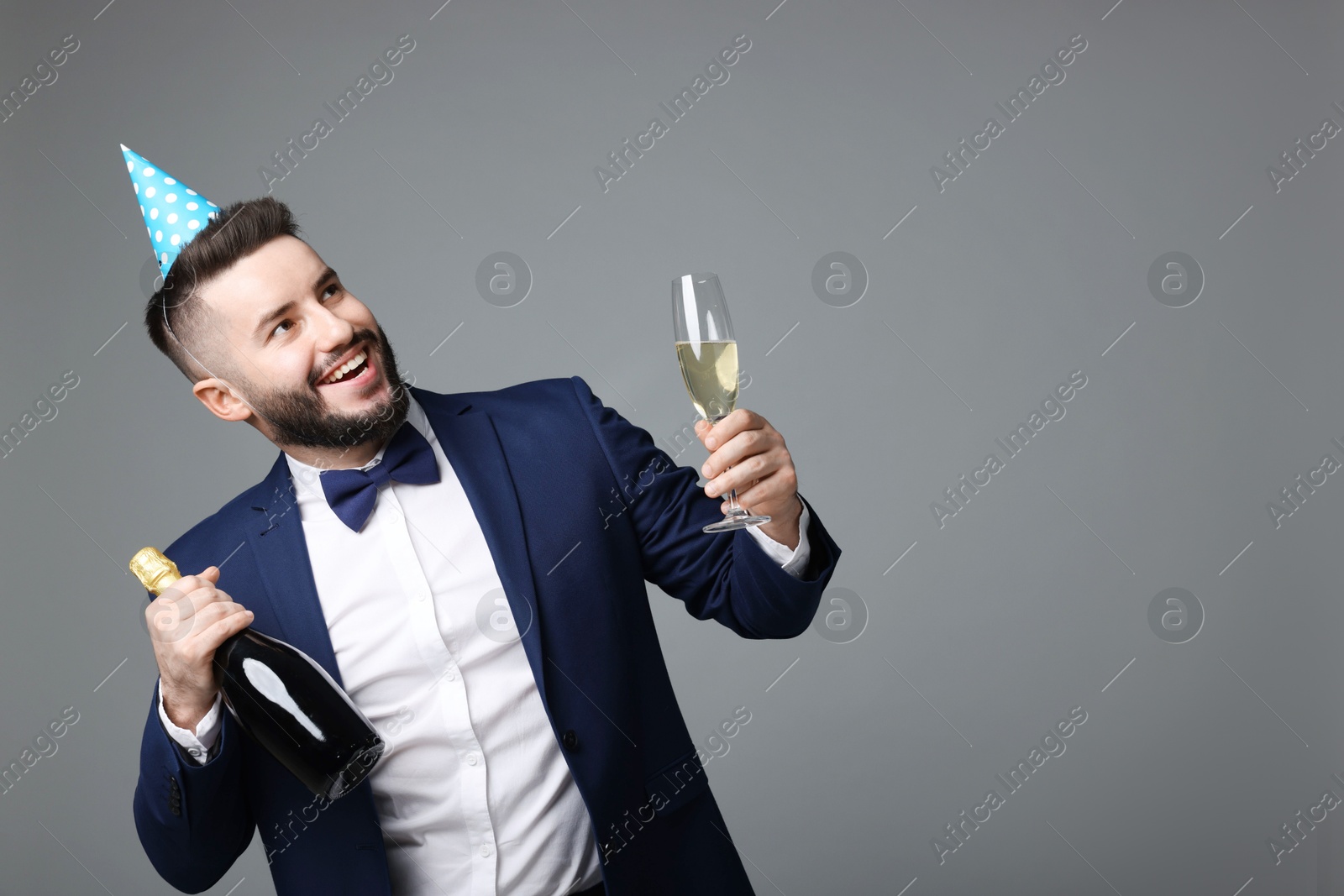 Happy Birthday. Handsome man with party hat and champagne on grey background, space for text Photo of Happy Birthday. Handsome man with party hat and champagne on grey background, space for text