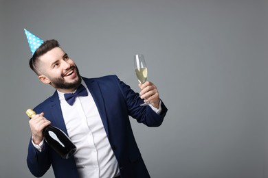 Photo of Happy Birthday. Handsome man with party hat and champagne on grey background, space for text
