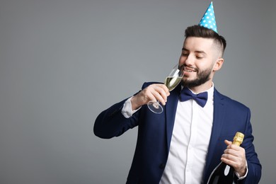 Photo of Happy Birthday. Handsome man with party hat and champagne on grey background, space for text