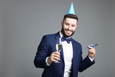 Photo of Happy Birthday. Handsome man with party hat, blower and glass of champagne on grey background
