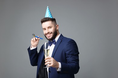 Photo of Happy Birthday. Handsome man with party hat, blower and glass of champagne on grey background
