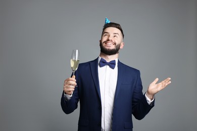 Photo of Happy Birthday. Handsome man with party hat and glass of champagne on grey background