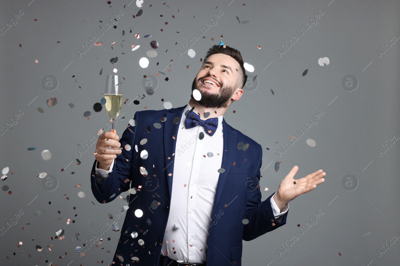 Happy Birthday. Handsome man with glass of champagne under confetti shower on grey background Photo of Happy Birthday. Handsome man with glass of champagne under confetti shower on grey background
