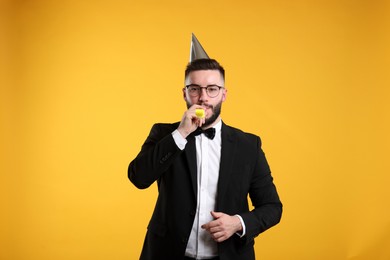 Photo of Happy Birthday. Handsome man with party hat and blower on orange background