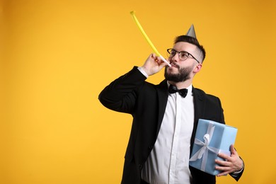 Photo of Happy Birthday. Handsome man with party hat, blower and gift box on orange background, space for text