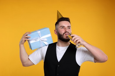 Photo of Happy Birthday. Handsome man with party hat, glass of champagne and gift box on orange background