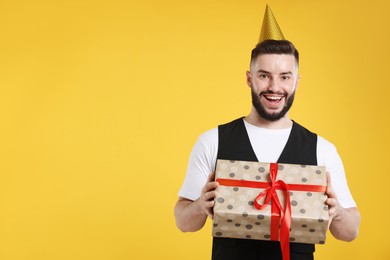 Photo of Happy Birthday. Handsome man with party hat and gift box on orange background, space for text