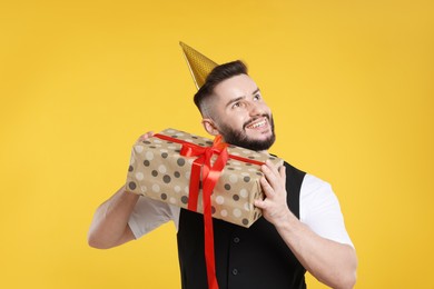Photo of Happy Birthday. Handsome man with party hat and gift box on orange background
