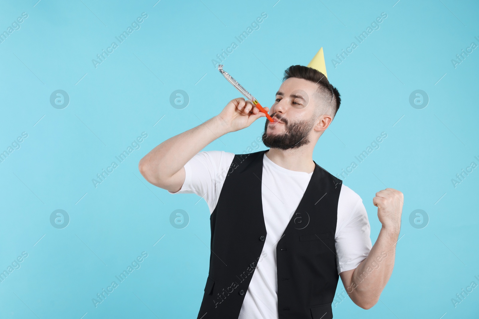 Happy Birthday. Handsome man with party hat and blower on light blue background, space for text Photo of Happy Birthday. Handsome man with party hat and blower on light blue background, space for text