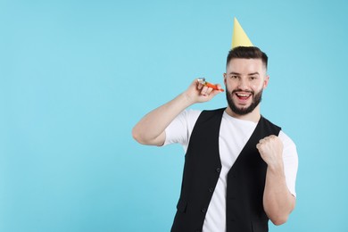 Photo of Happy Birthday. Handsome man with party hat and blower on light blue background, space for text