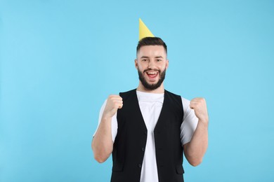 Photo of Happy Birthday. Handsome man with party hat on light blue background, space for text