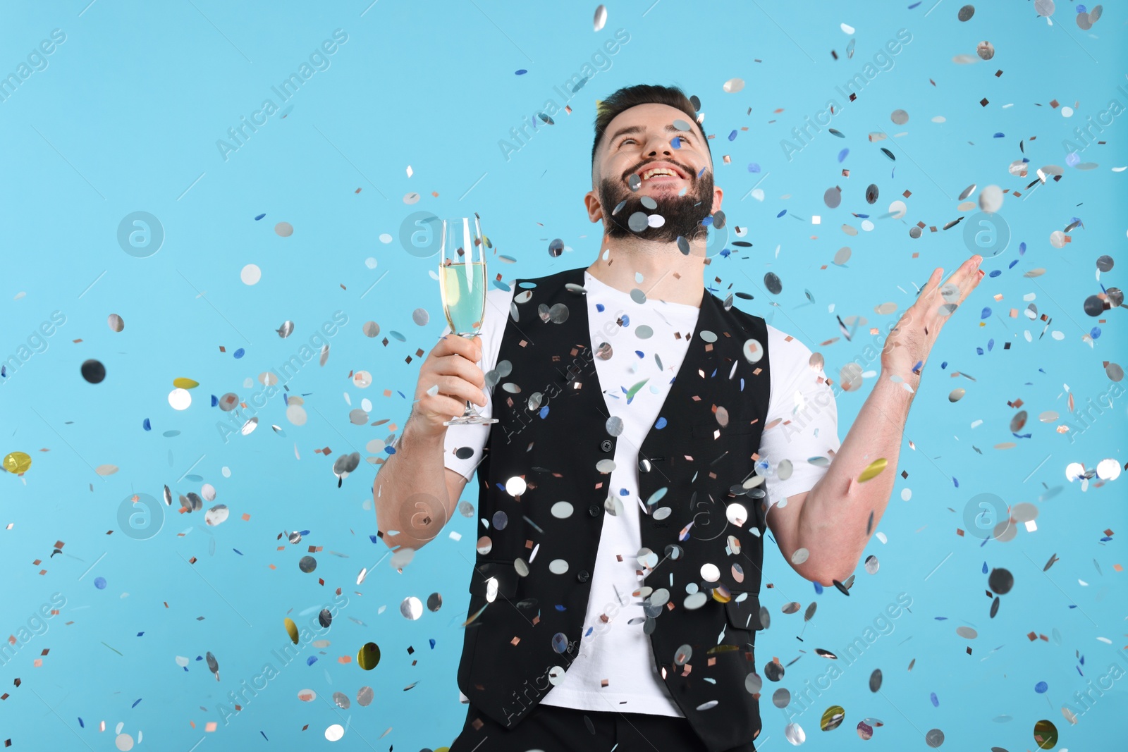 Happy Birthday. Handsome man with glass of champagne under confetti shower on light blue background, space for text Photo of Happy Birthday. Handsome man with glass of champagne under confetti shower on light blue background, space for text
