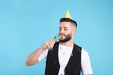 Photo of Happy Birthday. Handsome man with party hat and glass of champagne on light blue background