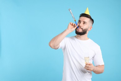 Photo of Happy Birthday. Handsome man with party hat, blower and glass of champagne on light blue background, space for text