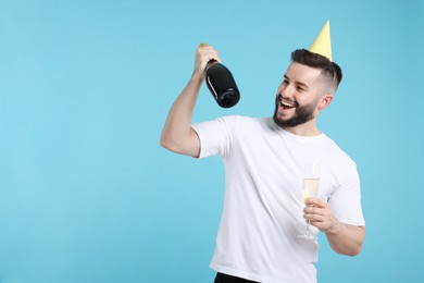 Photo of Happy Birthday. Handsome man with party hat and champagne on light blue background, space for text