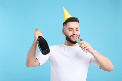 Photo of Happy Birthday. Handsome man with party hat and champagne on light blue background