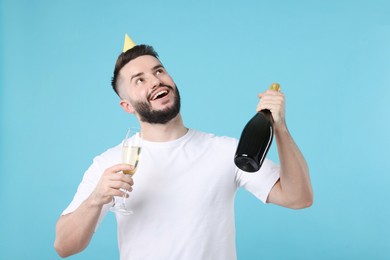 Photo of Happy Birthday. Handsome man with party hat and champagne on light blue background