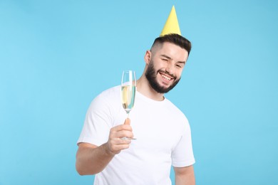 Photo of Happy Birthday. Handsome man with party hat and glass of champagne on light blue background