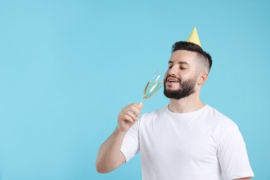 Photo of Happy Birthday. Handsome man with party hat and glass of champagne on light blue background, space for text