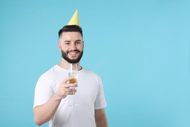 Photo of Happy Birthday. Handsome man with party hat and glass of champagne on light blue background, space for text