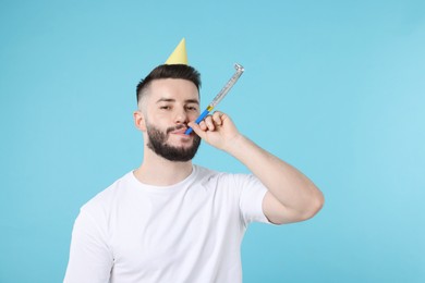 Photo of Happy Birthday. Handsome man with party hat and blower on light blue background, space for text