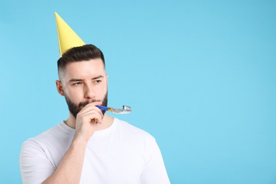 Photo of Happy Birthday. Handsome man with party hat and blower on light blue background, space for text