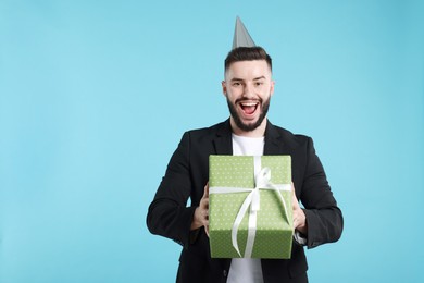 Photo of Happy Birthday. Handsome man with party hat and gift box on light blue background, space for text