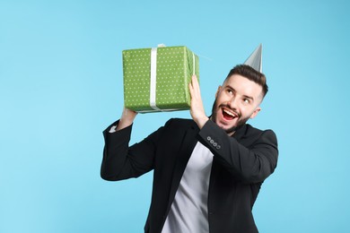 Photo of Happy Birthday. Handsome man with party hat and gift box on light blue background