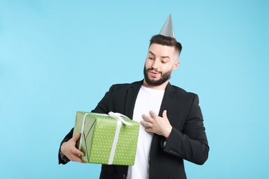 Photo of Happy Birthday. Handsome man with party hat and gift box on light blue background
