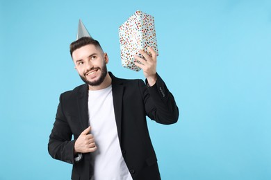 Photo of Happy Birthday. Handsome man with party hat and gift box on light blue background, space for text