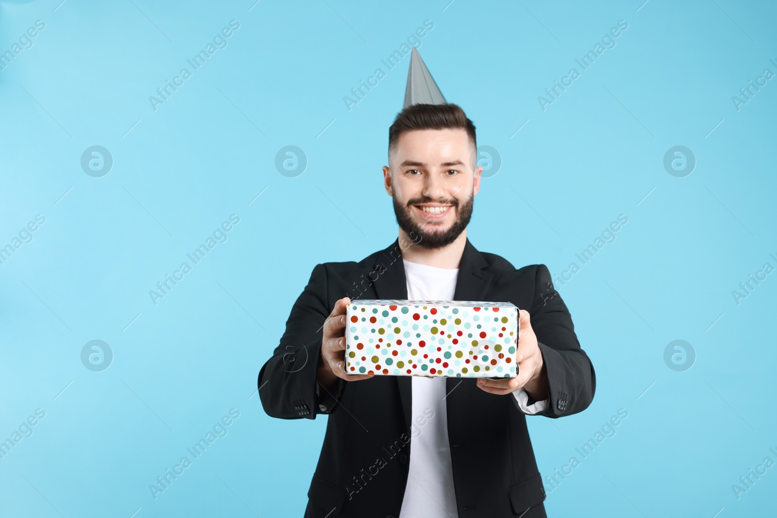 Happy Birthday. Handsome man with party hat and gift box on light blue background Photo of Happy Birthday. Handsome man with party hat and gift box on light blue background