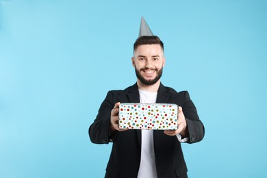 Photo of Happy Birthday. Handsome man with party hat and gift box on light blue background