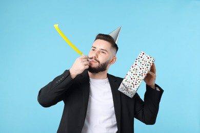 Photo of Happy Birthday. Handsome man with party hat, blower and gift box on light blue background