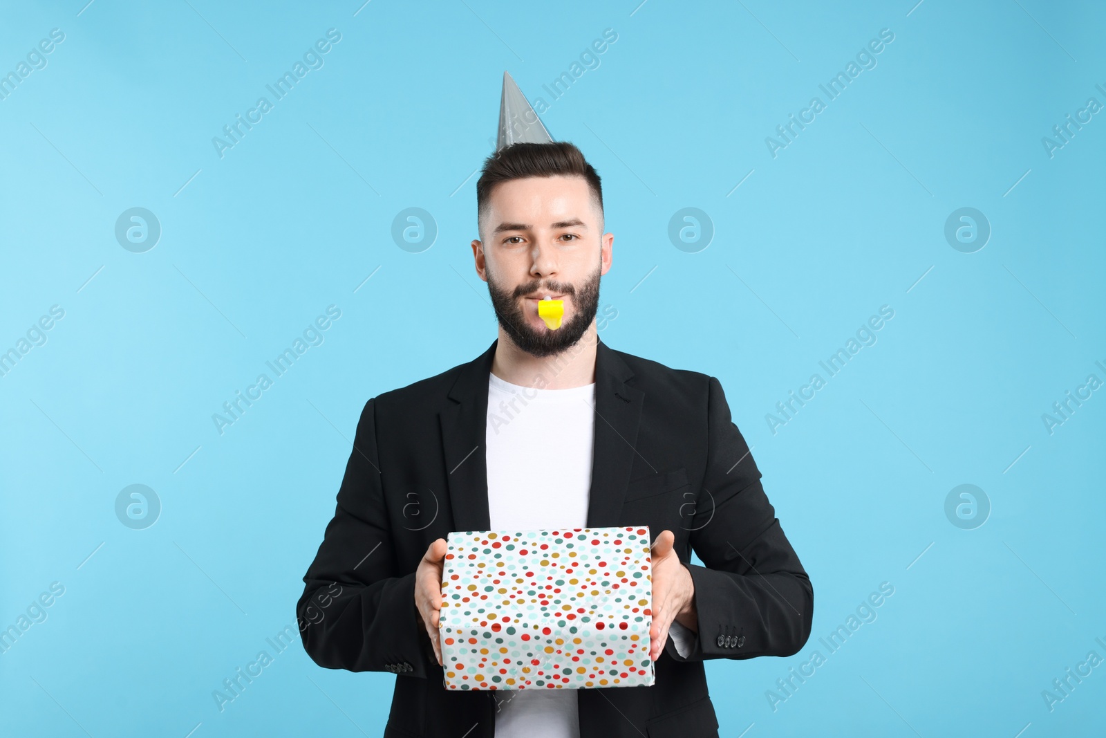 Happy Birthday. Handsome man with party hat, blower and gift box on light blue background Photo of Happy Birthday. Handsome man with party hat, blower and gift box on light blue background