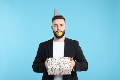 Photo of Happy Birthday. Handsome man with party hat, blower and gift box on light blue background