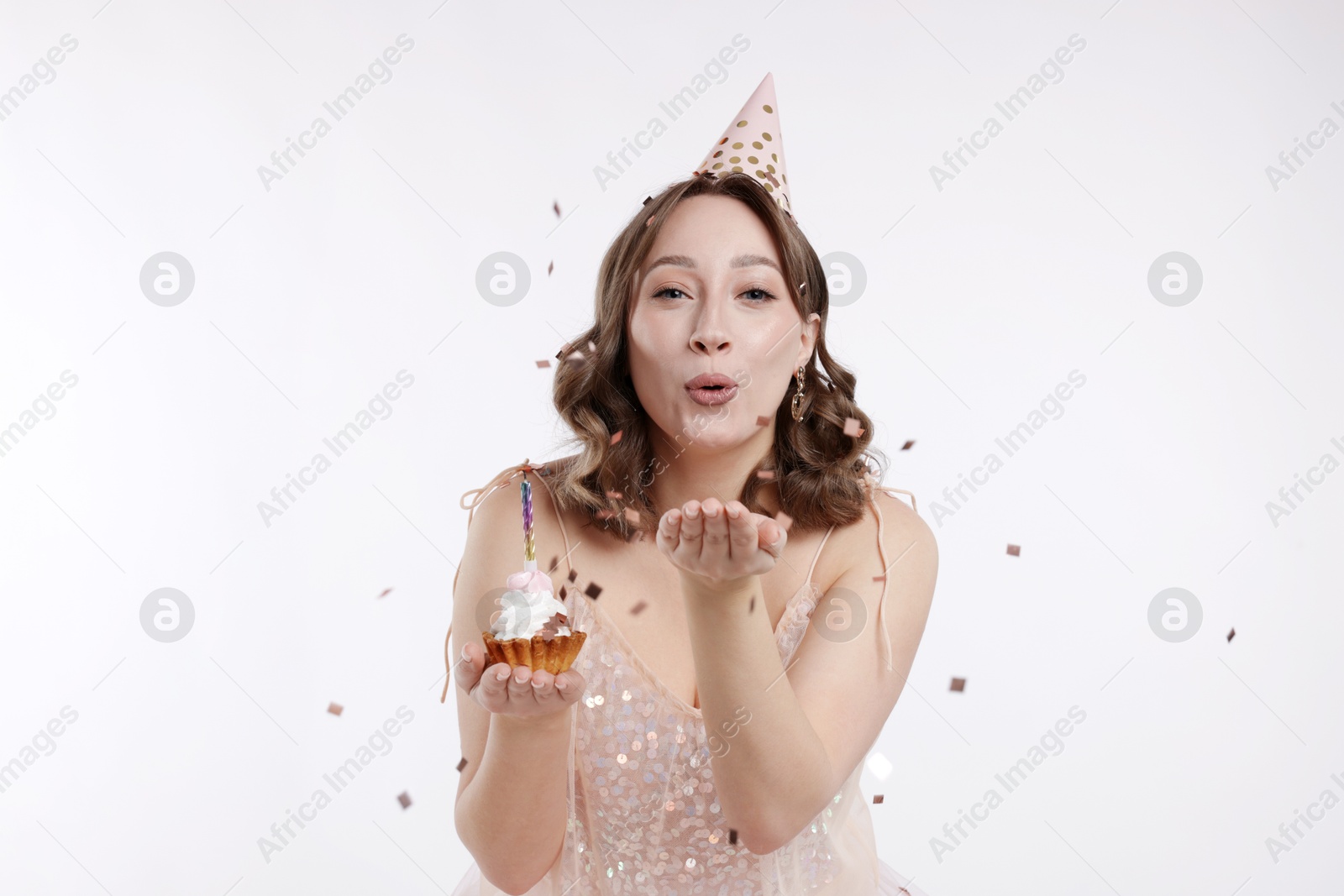 Birthday celebration. Woman blowing candle on cupcake and confetti against white background Photo of Birthday celebration. Woman blowing candle on cupcake and confetti against white background