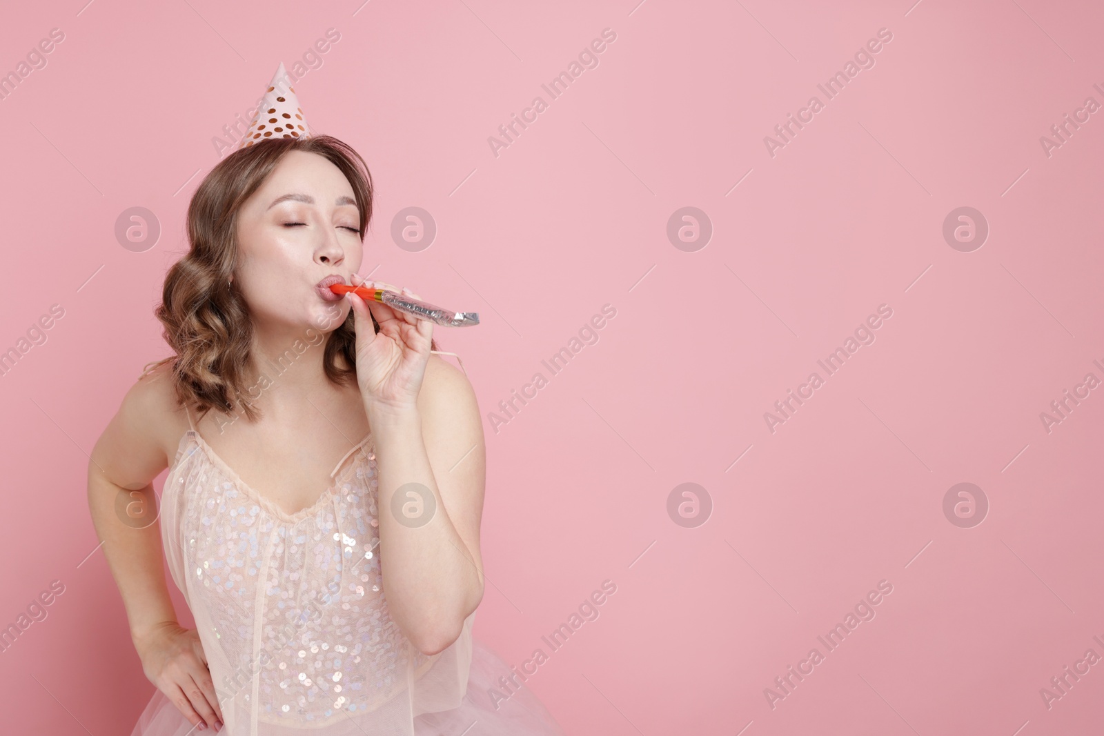 Birthday celebration. Woman with party horn on pink background. Space for text Photo of Birthday celebration. Woman with party horn on pink background. Space for text