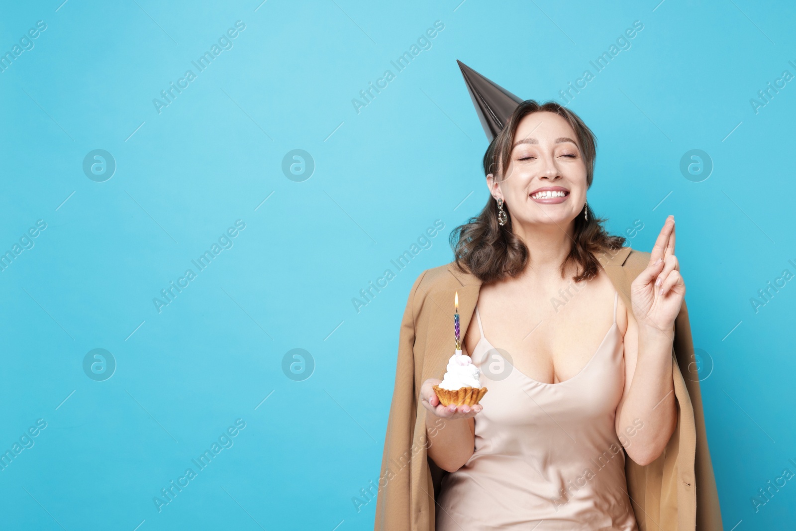 Birthday celebration. Woman with cupcake making wish on light blue background. Space for text Photo of Birthday celebration. Woman with cupcake making wish on light blue background. Space for text