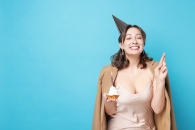 Photo of Birthday celebration. Woman with cupcake making wish on light blue background. Space for text