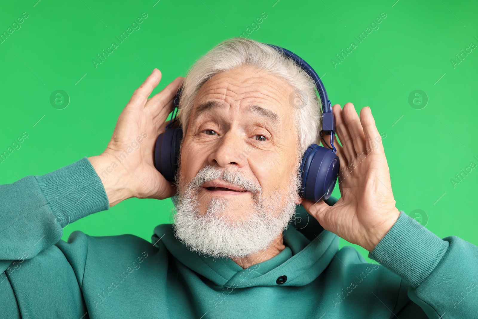Elderly man in headphones on green background Photo of Elderly man in headphones on green background