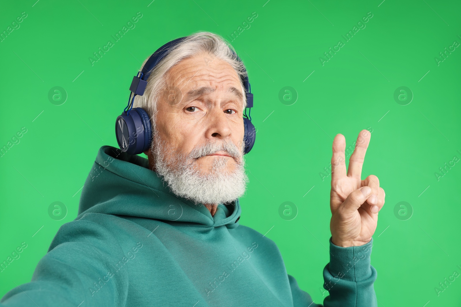 Elderly man in headphones taking selfie on green background Photo of Elderly man in headphones taking selfie on green background