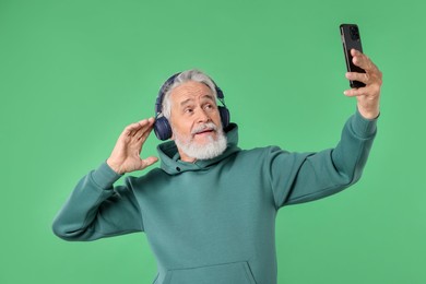 Photo of Elderly man in headphones taking selfie on green background