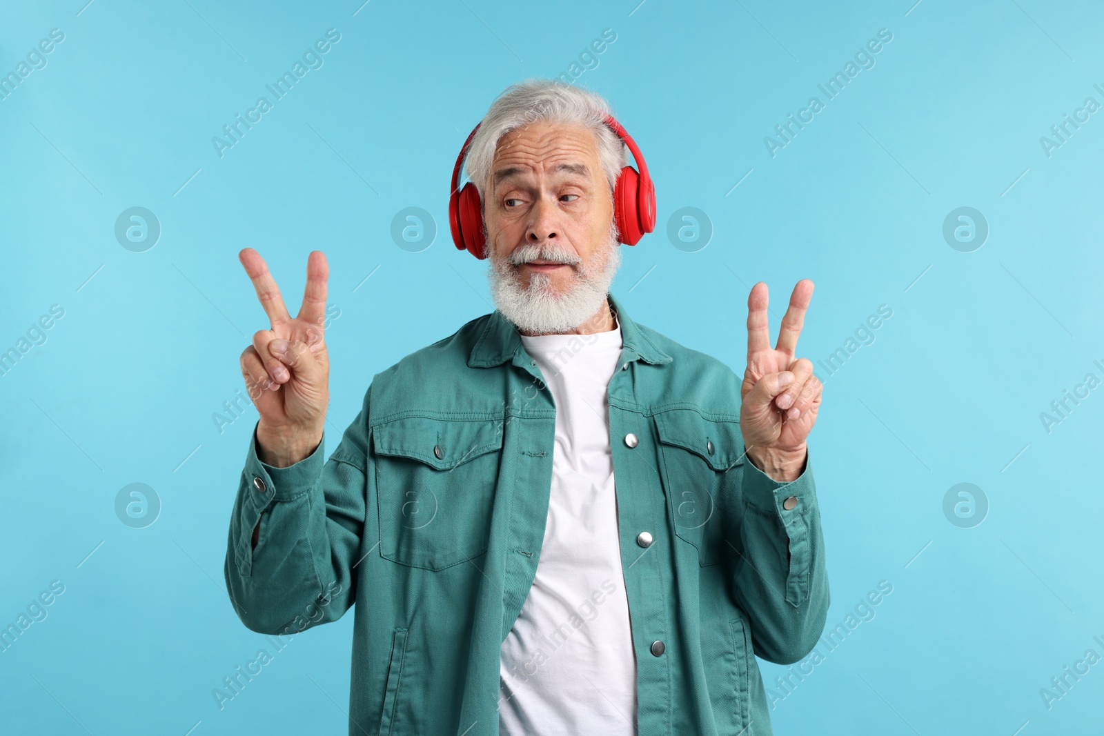 Elderly man in headphones showing peace signs on light blue background Photo of Elderly man in headphones showing peace signs on light blue background
