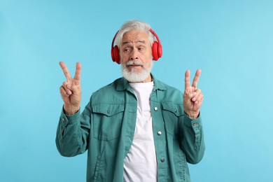 Photo of Elderly man in headphones showing peace signs on light blue background
