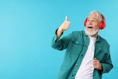 Photo of Elderly man in headphones showing thumbs up on light blue background, space for text